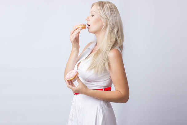 Young blonde woman in white dress holds in hands 2 pink donut with frosting - Фото, изображение