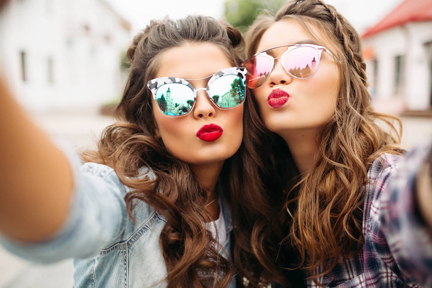 hinreißende brünette Freundinnen mit Frisur, verspiegelter Sonnenbrille und roten Lippen machen Selfie mit Entengesicht. - Foto, Bild