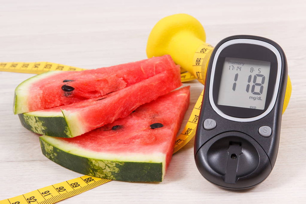 Watermelon, glucose meter with result of sugar level, tape measure and dumbbells for fitness, concept of healthy lifestyles, nutrition and slimming - Photo, Image