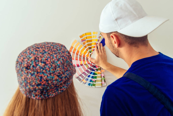 Cute young couple holding color guide on wall in living room - Photo, Image