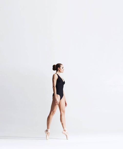 Ballerina in point shoes and bodysuit is dancing in studio. Young and graceful female ballet dancer. - Fotografie, Obrázek