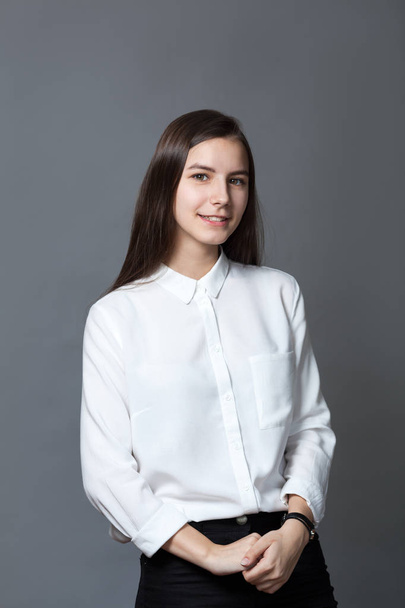 Portrait of happy nice schoolgirl teenager in white shirt on gray background, studio - Fotó, kép