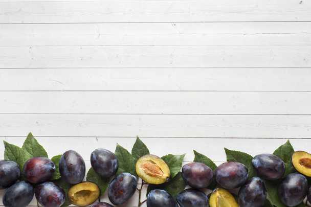 Fresh plum fruit with leaves on a light table - Fotó, kép