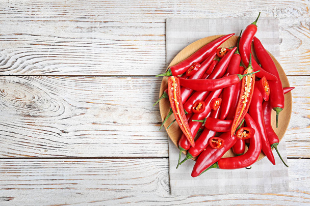 Plate with chili peppers on wooden background, top view - Fotoğraf, Görsel