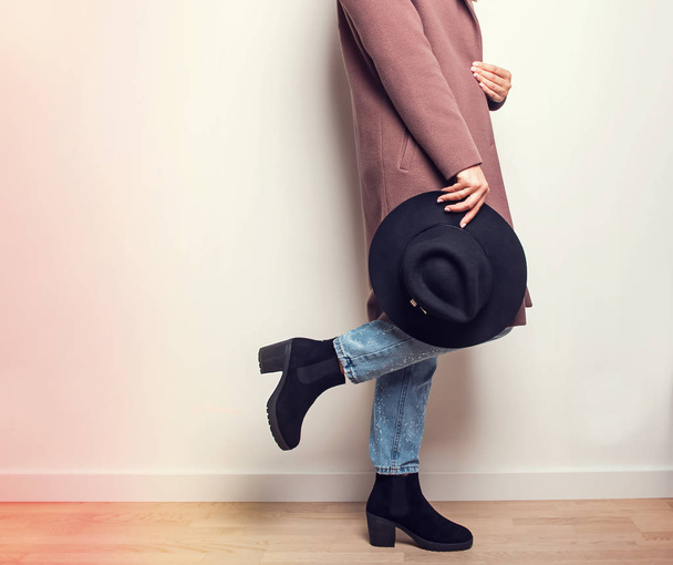 Autumn fashion. Woman in beige coat and stylish boots holding a hat in hand. - Foto, imagen