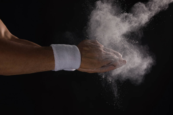 Young man applying chalk powder on hands against dark background - Photo, image