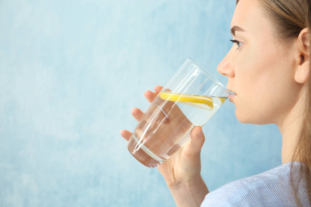 Young woman drinking water with lemon against color background - Foto, afbeelding