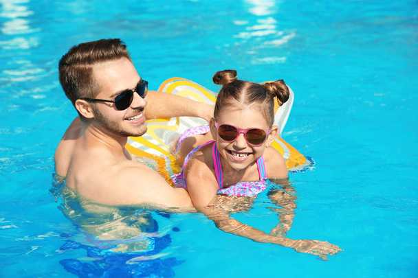 Father teaching daughter to swim with inflatable star in pool on sunny day - Фото, зображення