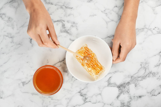 Woman pouring honey onto fresh honeycomb at marble table, top view - Photo, Image