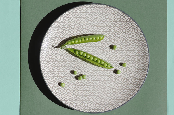 frische grüne Erbsen auf einem Teller auf grünem Hintergrund - Foto, Bild