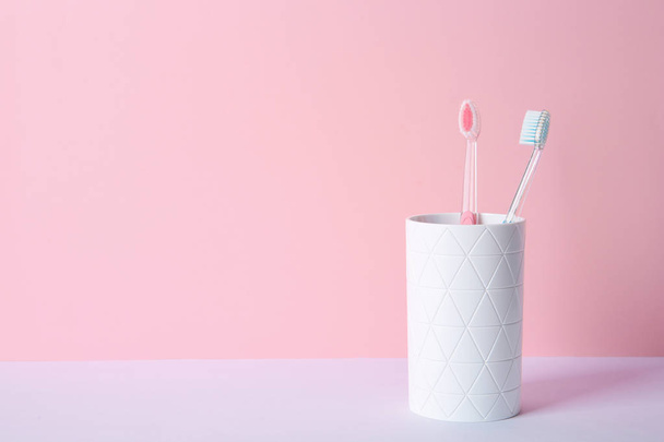Cup with toothbrushes on table against color background. Dental care - Φωτογραφία, εικόνα