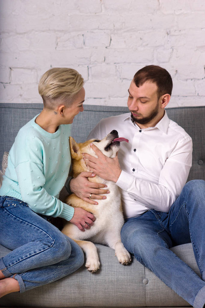 Beautiful young family with dog sits on sofa - Fotó, kép