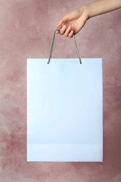 Woman holding paper shopping bag on color background - Foto, afbeelding