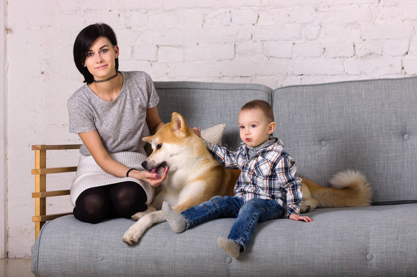 Beautiful mother and son with dog sits on sofa - Photo, Image