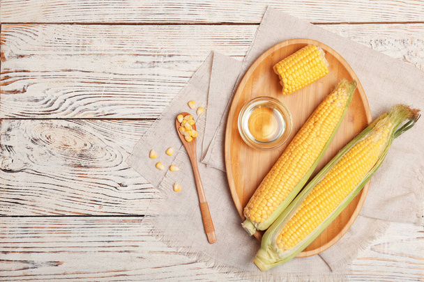 Flat lay composition with corn cobs and bowl of oil on wooden background - Fotoğraf, Görsel