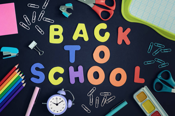 In the center of a black background with colored letters lined inscription Back to School. Around are stationery and school supplies. Beautiful picture from above, layout. - Photo, Image