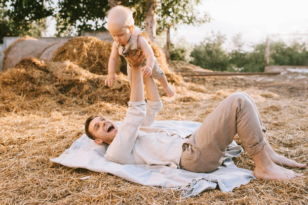 happy father holding little son while resting on hay in village - Photo, Image