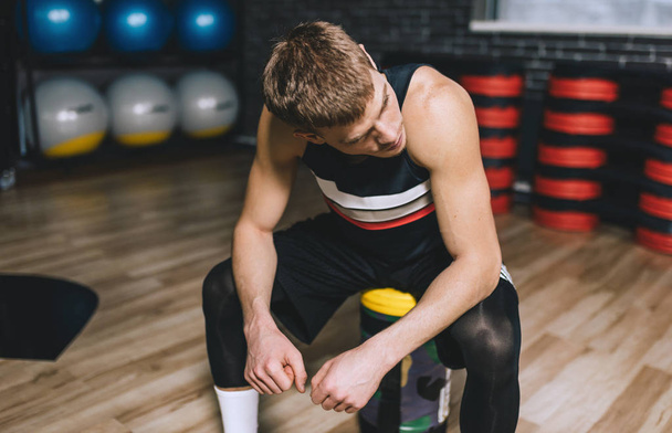 Sporty man sitting on sandbag relaxing after exercises in the gym. Attractive athletic male rest after hard workout with weight training with copy space for your text or advertising. - Fotografie, Obrázek