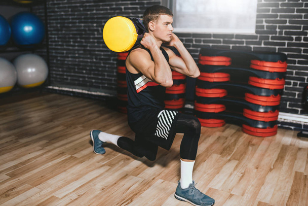 Handsome sportsman with sandbag on shoulders while exercises in the gym. Attractive athletic male doing hard workout with weight training with copy space for your text or advertising. Sport concept. - Foto, imagen