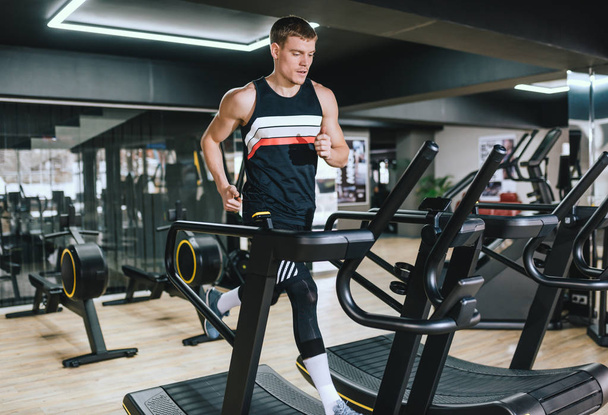 Athletic man running in a modern gym on a treadmill doing cardio exercises. Young handsome fit man running on treadmill in the fitness club. Sport, fitness, healthy life and people concept. - 写真・画像