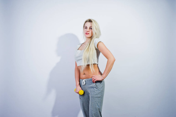 Blonde sporty girl with yellow dumbbell posed at studio against white background. - Fotó, kép
