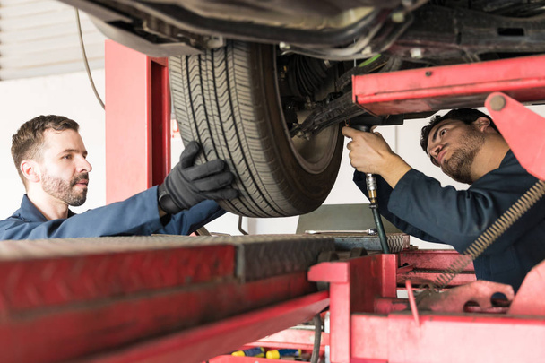 Medio adulto compañeros de trabajo que trabajan en el neumático del coche en taller de reparación de automóviles
 - Foto, imagen