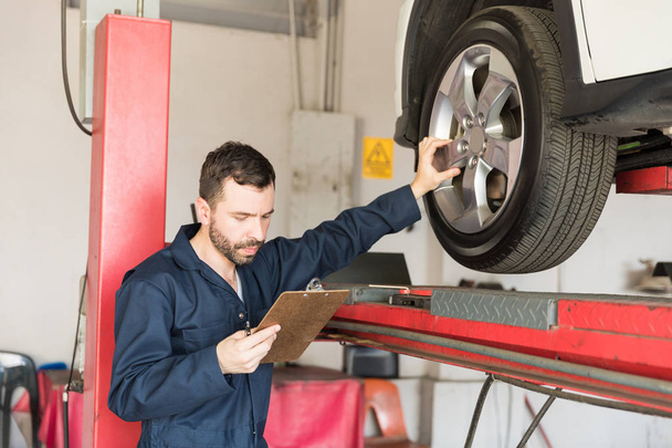 Ingénieur automobile adulte moyen examinant le pneu de voiture tout en passant par la liste de contrôle en atelier
 - Photo, image