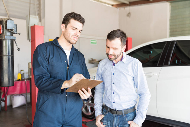 Mecánico de coche adulto medio mostrando lista de verificación de mantenimiento para el cliente masculino en el garaje
 - Foto, Imagen