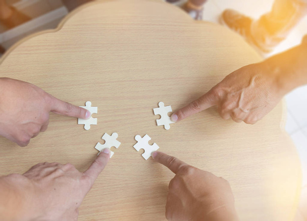 ヘルプ サポート、チームワークの概念のための木のテーブル背景に一緒にパズルのピースを配置したいのジグソー パズルを組み立てるビジネス人々 のグループ - 写真・画像