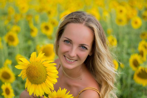Happy woman with sunflowers. The girl in the fields of a sunflower. Beautiful girl resting in the summer at sunset. Woman in a field of blooming sunflowers. Summer walks in nature. Recreation. Sunflower at sunset - Photo, Image