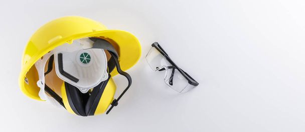 Protective earmuffs and face mask in hard hat alongside safety goggles on white background with copy space banner image - Photo, Image