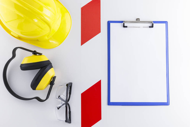 Red and white barricade tape between safety gear including hard hat, earmuffs, and goggles and a clipboard with blank sheet - Photo, Image