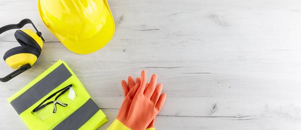 Imagen de la pancarta del equipo de seguridad de construcción que incluye un sombrero duro, una chaqueta reflectante plegada, gafas y guantes de goma planos sobre una superficie de madera blanca con espacio para copiar
 - Foto, imagen