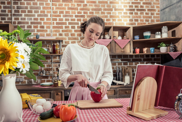 concentrated adult housewife cutting red bell pepper at kitchen - Photo, Image