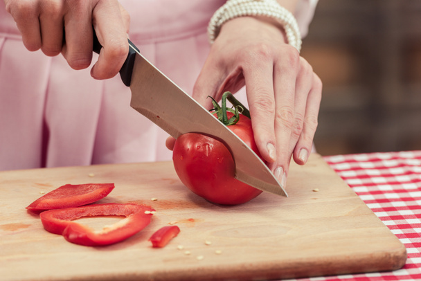 bijgesneden schot van huisvrouw cutitng tomaat op houten snijplank - Foto, afbeelding