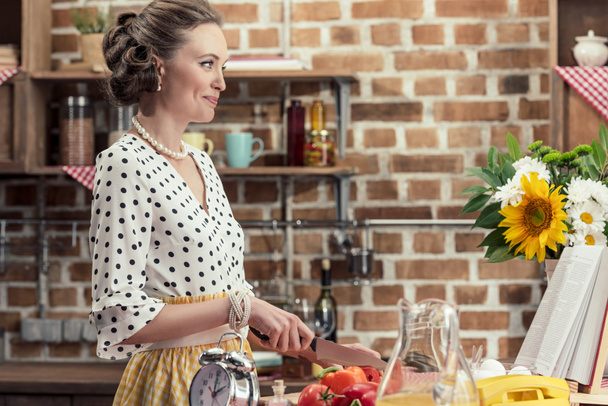 hymyilevä aikuinen kotiäiti leikkaa vihanneksia ja katselee pois keittiöön
 - Valokuva, kuva