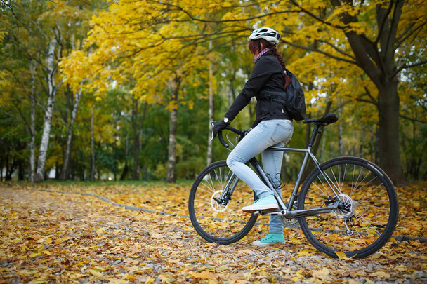 Photo of girl in helmet riding bicycle in autumn forest - Foto, afbeelding