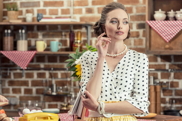 thoughtful adult housewife in vintage clothes looking away at kitchen - Foto, afbeelding