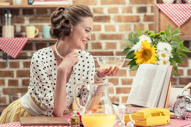 sorridente casalinga adulta con ciotola lettura libro di ricette in cucina
 - Foto, immagini