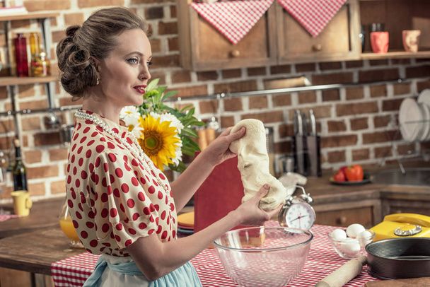 Seitenansicht einer erwachsenen Hausfrau, die Teig knetet und in die Küche schaut - Foto, Bild