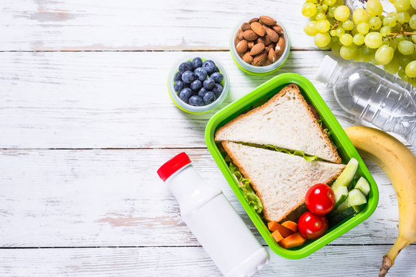 De doos van de lunch met sandwich, fruit, yoghurt, noten en bessen. - Foto, afbeelding