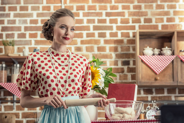 sorridente casalinga adulta con mattarello guardando lontano in cucina
 - Foto, immagini