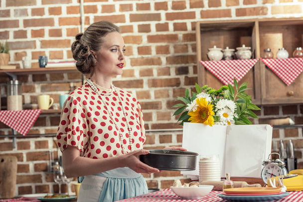 kaunis aikuinen kotiäiti leivontaan trey kakku katselee pois keittiöön
 - Valokuva, kuva