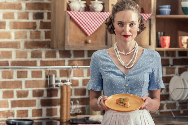 atractiva ama de casa adulta con pastel recién horneado mirando a la cámara en la cocina
 - Foto, imagen