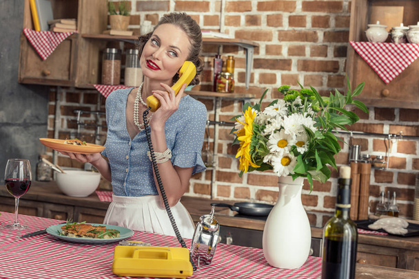 beautiful adult housewife with freshly baked cake talking by vintage rotary phone at kitchen - Fotoğraf, Görsel