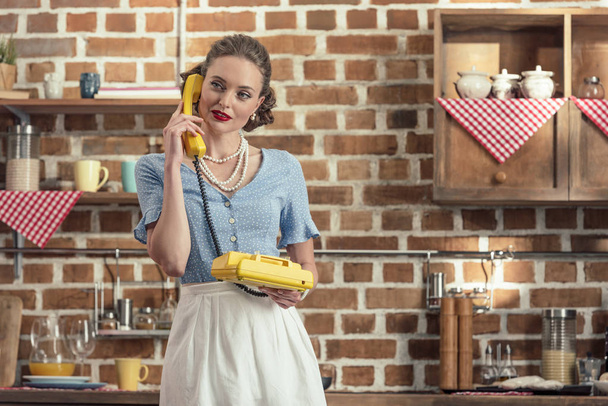 attractive adult housewife talking by vintage rotary phone at kitchen - Foto, imagen