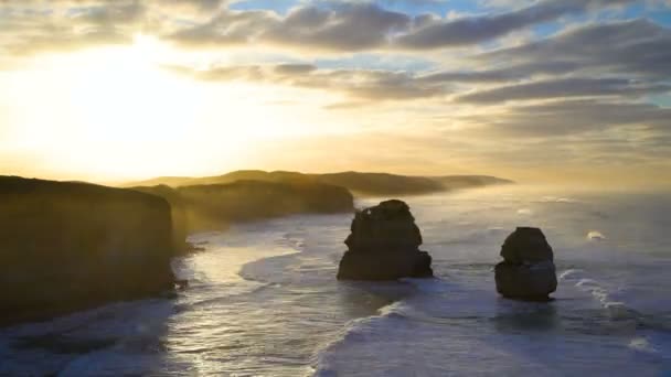 Timelapse ochtendzon door wolken en de oceaan golven rond kalkstenen rotsformaties voor de kust van de twaalf apostelen Victoria Australië - Video