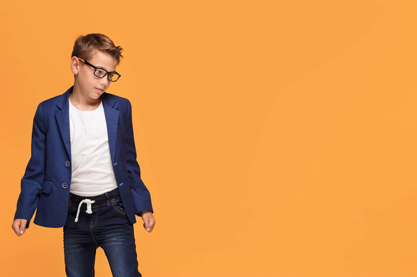 Little elegant boy posing on orange studio backgroud, wearing fashionable eyeglasses and jacket. - Foto, Imagen