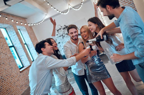 Let the party begin! Group of young people having fun together. Dancing in big light room with champagne. Celebrating holiday in big company of close friends. - Фото, зображення
