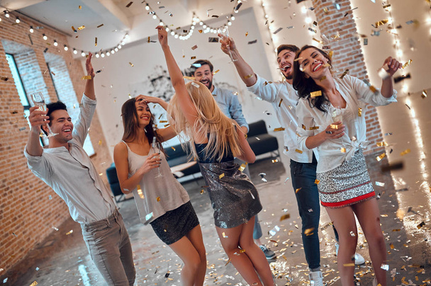 Let the party begin! Group of young people having fun together. Dancing in big light room with champagne and confetti falling. Celebrating holiday in big company of close friends. - Photo, image
